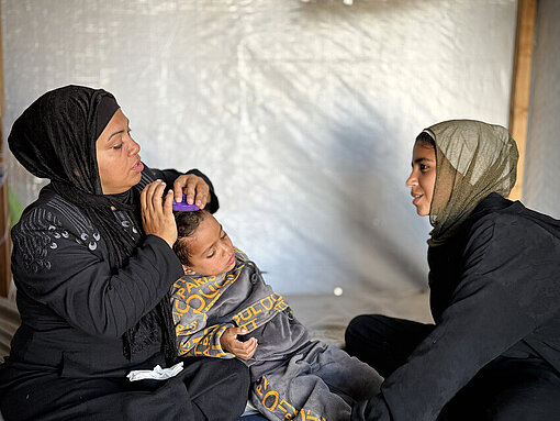 Latifah mit ihrem Sohn und ihrer Tochter Eine Mutter aus Gaza mit ihren Kindern zwei Kindern, eine junge Frau und ein kleiner Junge, sitzen in einem Zelt auf dem Boden