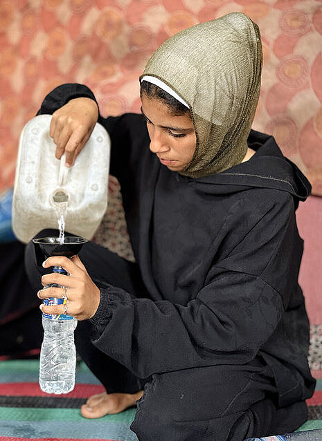 Latifahs Tochter füllt Plastikflaschen mit Wasser auf Eine junge Frau befüllt mit einem Kanister Wasserflaschen aus Plastik