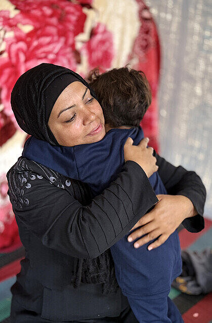 Mutter Latifah umarmt liebevoll ihren vierjährigen Sohn Eine Mutter mit Kopftuch kniet in einem Zelt auf dem Boden und nimmt ihr Kind liebevoll in den Arm