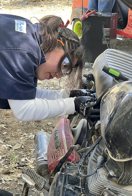 Claudia repariert ein Motorrad in der Werkstatt ihres Onkels Eine junge Frau schraubt mit Schutzbrille und Arbeitskleidung ausgestattet an einem Motorrad