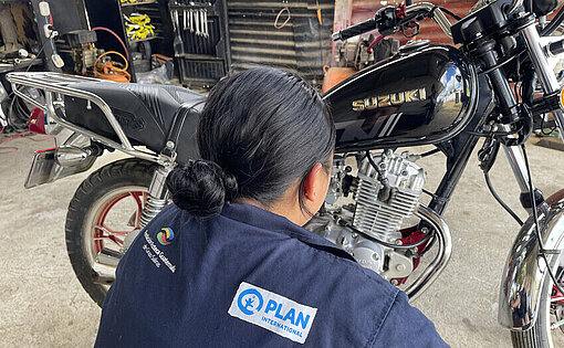 Claudia hatte schon immer ein Faible für Motorräder Eine junge Frau in Blaumann hockt vor einem schwarzen Motorrad