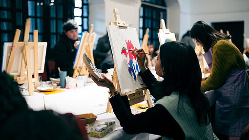 Teilnehmerinnen des Kunst-Workshops in Nepal Junge Menschen malen konzentriert auf Leinwänden in einem großen Raum