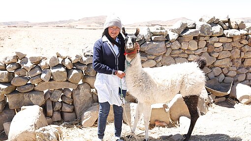 Lamas für Jugendliche in Bolivien Eine Frau steht neben einem Lama und hält es an der Leine. Sie grinst in die Kamera.