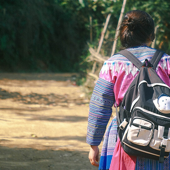 Mädchen mit Rucksack geht einen Weg entlang, Foto von hinten