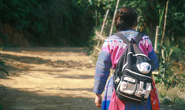 Mädchen mit Rucksack geht einen Weg entlang, Foto von hinten