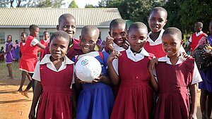 Eine Gruppe von Mädchen aus Malawi steht Freude strahlend zusammen. Sie tragen die Uniformen ihrer Schule und halten einen Fußball in die Kamera.