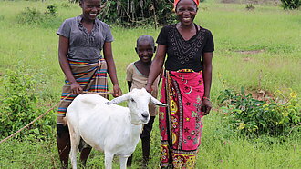 Ziegen gegen Armut Eine Familie steht mit ihrer Ziege auf einer Wiese.