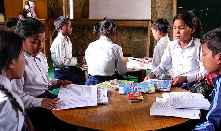 Vier Kinder sitzen an einem runden Tisch und lernen zusammen