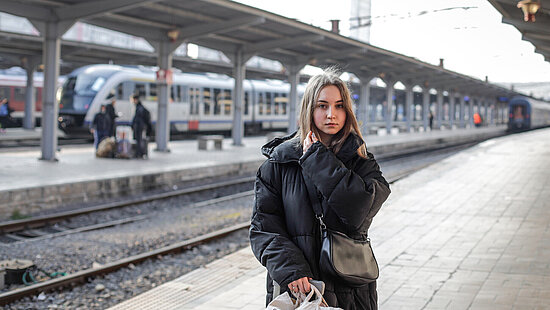 Eine junge Frau steht an einem Bahnhof