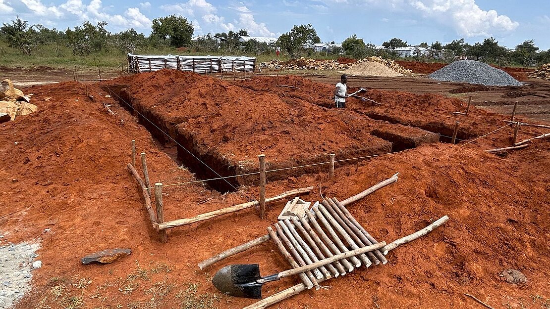 Das Fundament für ein neues Gebäude entsteht. Ein Quadratischer Graben ist gezogen. Es liegt Kies bereit.