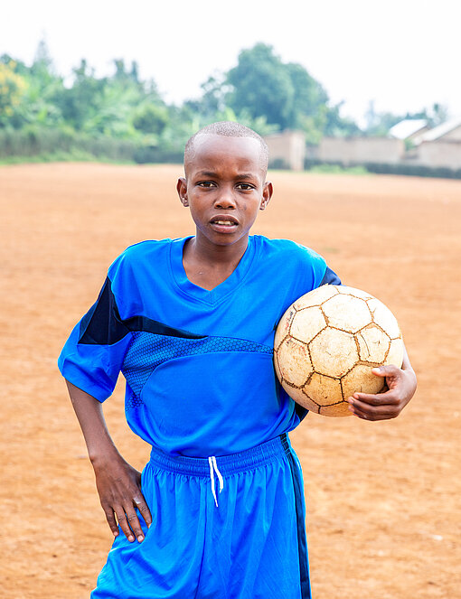 Junge im blauen Trikot mit einem Fußball unter dem Arm 