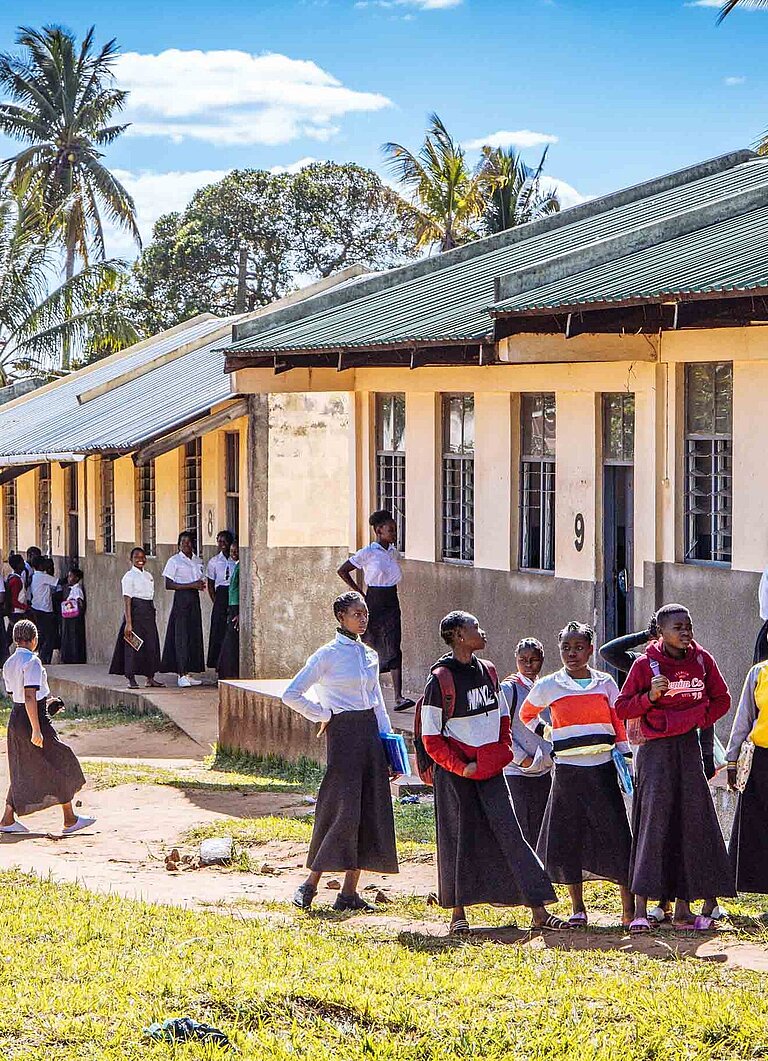 Mädchen und Jungen stehen vor einer Schule, die Plan International in Mosambik gebaut hat