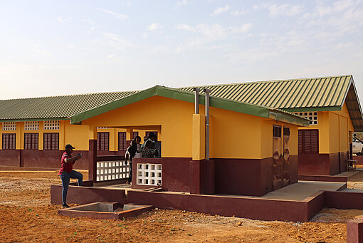 Gelb-braunes, neues Schulgebäude mit einigen Menschen im Hintergrund