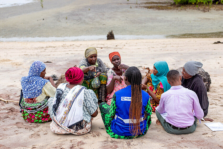 Eine Gruppe Frauen sitzt im Kreis am Strand und diskutiert