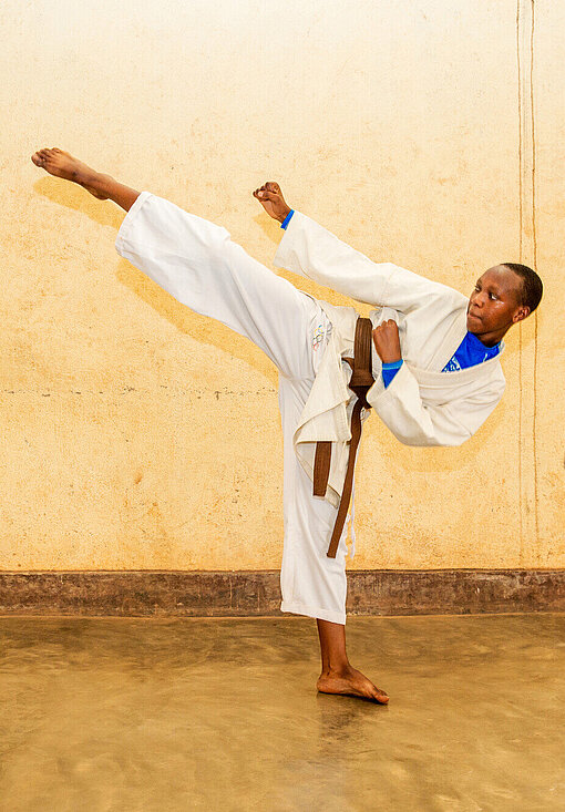 Eine junge Frau in Karate-Anzug macht einen High Kick