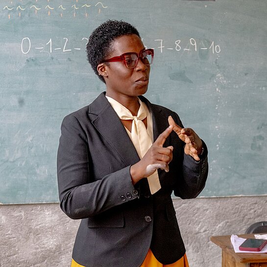 Rose erklärt ihrer Klasse geduldig, wie sie mit zehn Fingern zählen können Eine Lehrerin erklärt das Zehn-Finger-Zählsystem