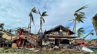 Abgeknickte Palmen, zerstörte Häuser, überall liegen Holzstücke auf dem Boden verstreut.