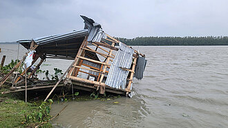 Die Überreste eines Hauses werden von einer Überschwemmung langsam in den Fluss gezogen.