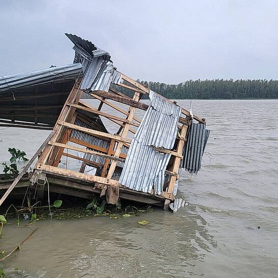 Die Überreste eines Hauses werden von einer Überschwemmung langsam in den Fluss gezogen.