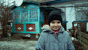 Junges Mädchen in Winterbekleidung steht vor einem Haus in der Ukraine
