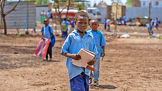 Ein Junge in blauer Hose und blauem Hemd trägt Schulbücher