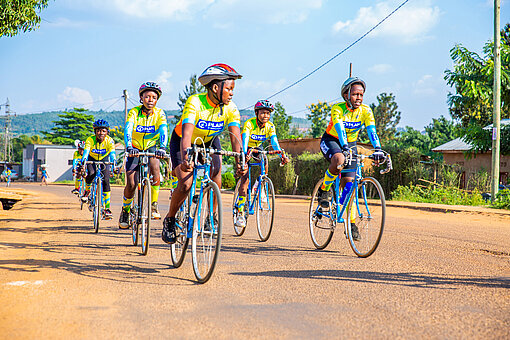 Eine Gruppe junger Frauen fährt nebeneinander mit dem Rennrad über die Straße, sie tragen alle die gleichen Trikots und Helme.