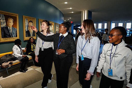 Vier Jugendliche laufen durch das Gebäude der Vereinten Nationen, an den Wänden hängen Porträts