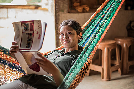 Eine junge Frau sitzt in einer Hängematte und liest in einem Prospekt