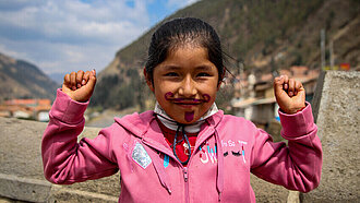 Ein junges Mädchen hat einen Bart ins Gesicht gemalt und hält zwei Fäuste in die Luft