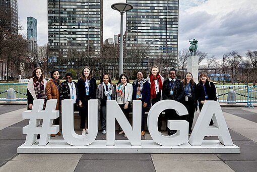 Eine Gruppe Menschen steht vor einem großen Schriftzug #UNGA