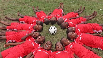 Kinder lachen und bilden auf dem Rasen einen Kreis um einen Fußball