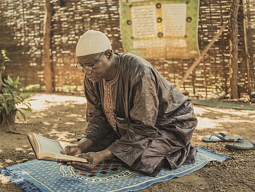 Kinda sitzt auf seinem Gebetsteppich und liest im Koran