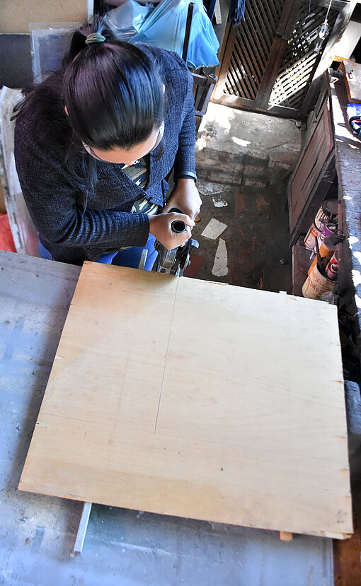 Frau sägt eine Holzplatte mit einer Kreissäge (Vogelperspektive)
