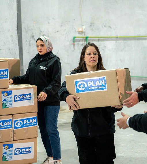 Mitarbeitende von Plan International tragen Kartons mit Plan-Logo
