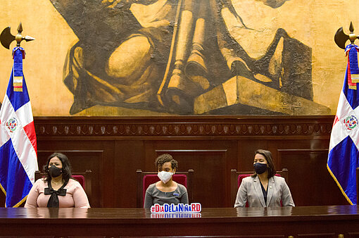 Drei Frauen sitzen im Nationalparlament, rechts und links sind Flaggen