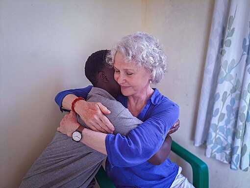 Eine junge tansanische Frau und eine ältere weiße Frau umarmen sich herzlich