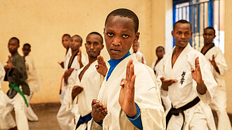 Eine Gruppe Jugendlicher in Karate-Anzügen schaut konzentriert in die Kamera, Hände gehoben.