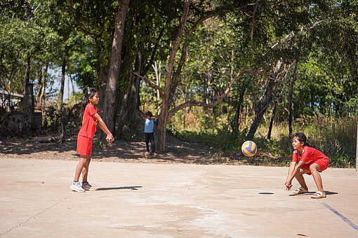 Zwei Mädchen in roten Trikots spielen sich einen Volleyball zu