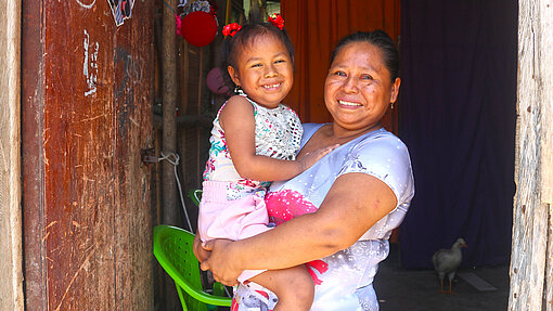 Mutter-Kind-Gesundheit Eine Mutter hält lächelnd ihre kleine Tochter auf dem Arm.