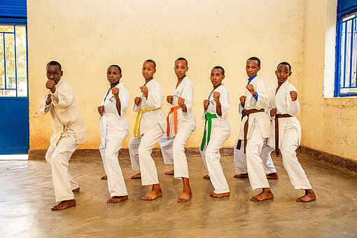 Sieben Jugendliche in Karate-Anzügen stehen in einer Reihe nebeneinander und haben die gleiche Haltung eingenommen: Gebeugte Knie und gehobene Fäuste.